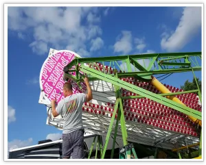 Worker installing a circular PINK sponsor sign on the Ferris wheel