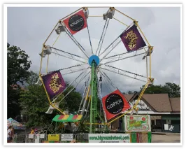 Daytime Ferris wheel with purple sponsor panels and a branded entrance sign